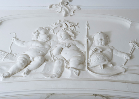 Putti verbeelden oorlog en vrede in het stucwerk boven de deur naar de zaal.