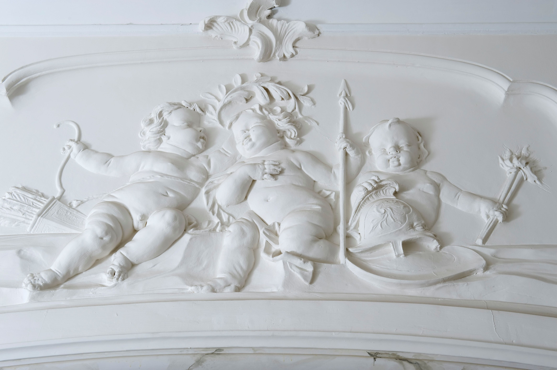 Putti verbeelden oorlog en vrede in het stucwerk boven de deur naar de zaal.